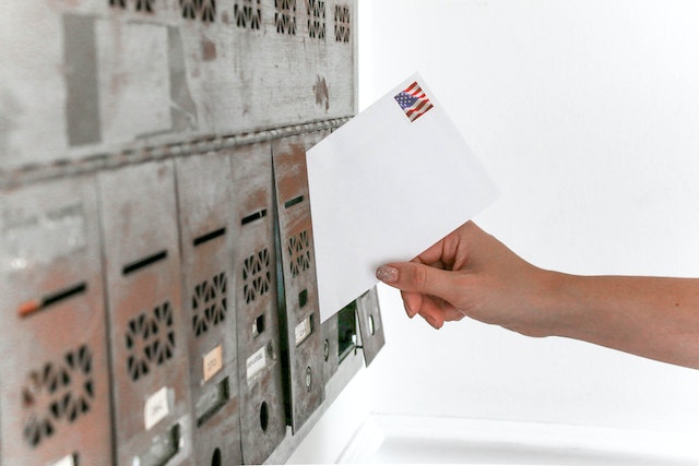 placing a white envelope with an US stamp into a silver community mailbox